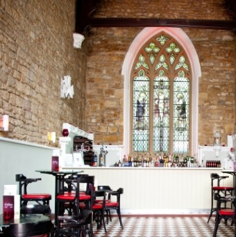 Intérieur de the 5 Church à Los Angeles : église transformée en restarant avec comptoir blanc, tables et chaises en rouge et noir et une grande fenêtre d'origine.