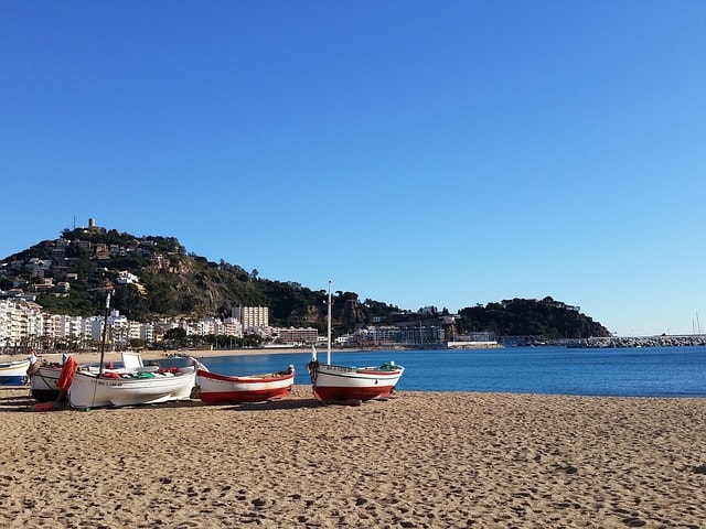 Plage de Costa Brava avec quelques barques, au fond, la ville et la montagne.