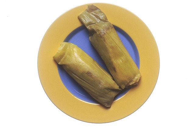 Deux tamales enveloppés dans des épis de maïs sur une assiette.