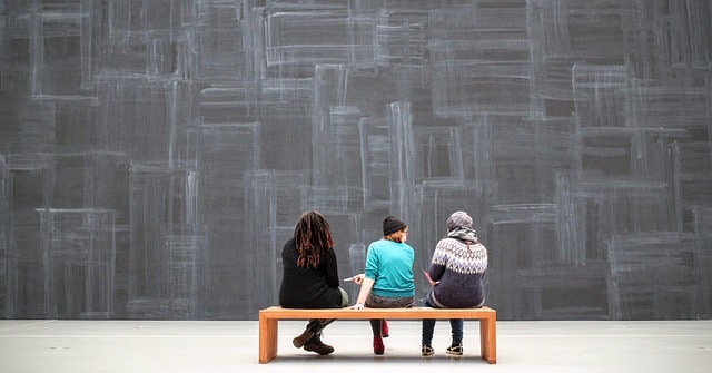 Trois femmes assises sur un banc dans un musée.