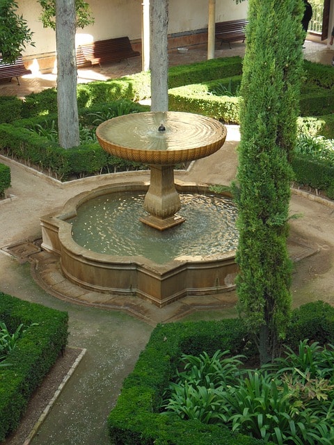 Fontaine trônant au milieu d'un jardin arboré.