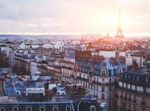 La ville de Paris prise en photo depuis les toits des immeubles Haussmanniens avec une éclaircie derrière la tour Eiffel.