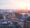 La ville de Paris prise en photo depuis les toits des immeubles Haussmanniens avec une éclaircie derrière la tour Eiffel.