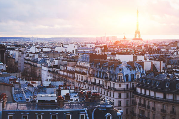 La ville de Paris prise en photo depuis les toits des immeubles Haussmanniens avec une éclaircie derrière la tour Eiffel.