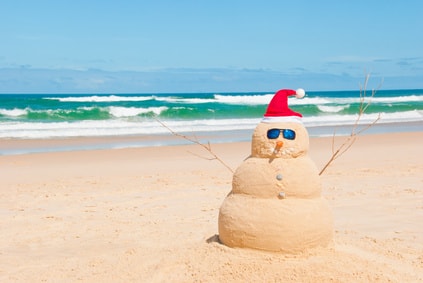 Un bonhomme de neige en sable sur une plage devant une mer verte. Top 20 des destinations Noël.