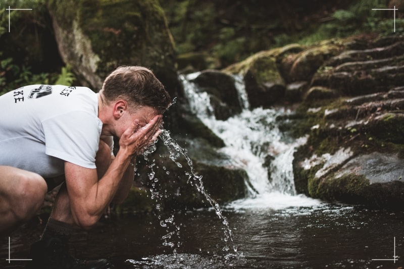Un jeune homme se rafraîchissant le visage dans un rivière.