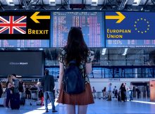 Une femme à l'aéroport se tenant devant deux panneaux indiquant des directions différentes pour le Brexit et l'Union Européenne.