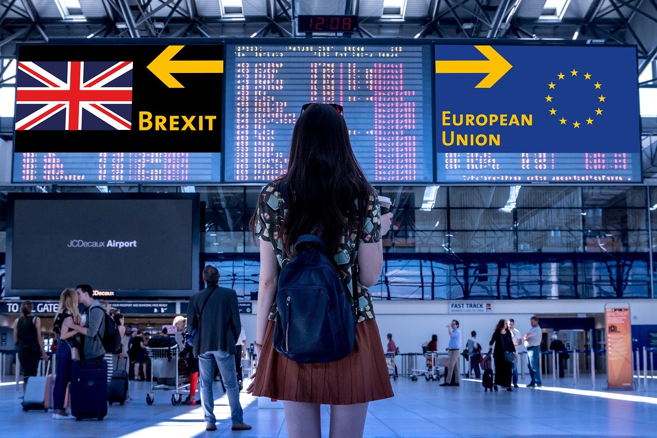 Une femme à l'aéroport se tenant devant deux panneaux indiquant des directions différentes pour le Brexit et l'Union Européenne.