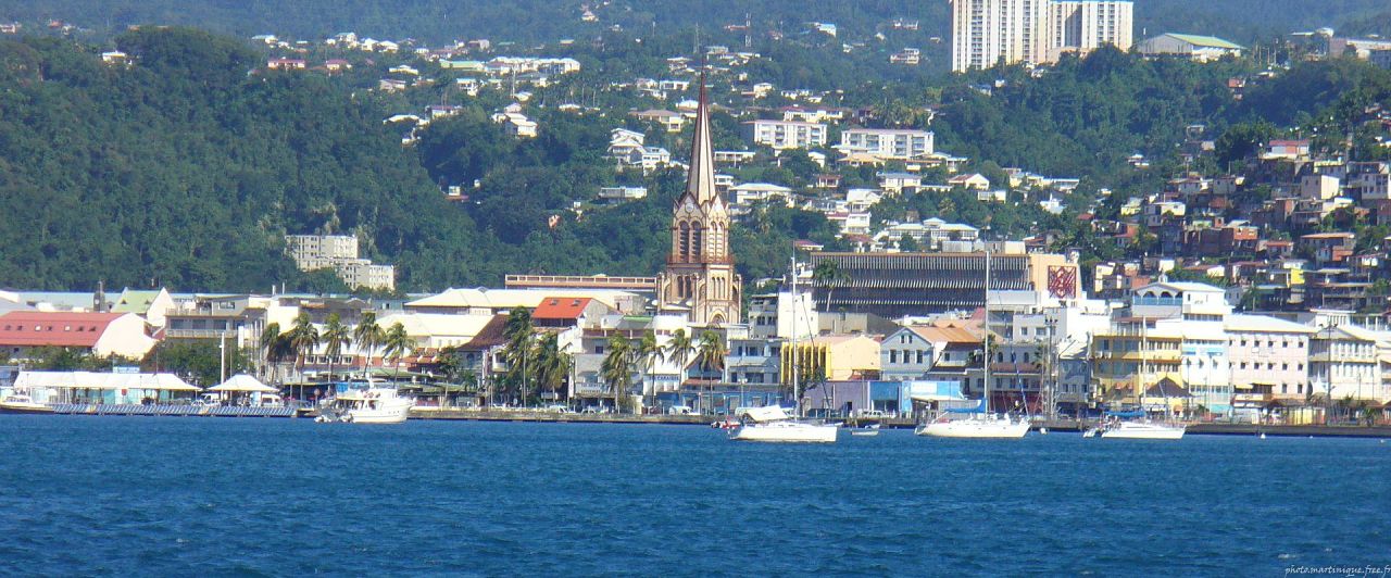 Un vol Fort de France pas cher avec Algofly illustré la ville et son église en front de mer.