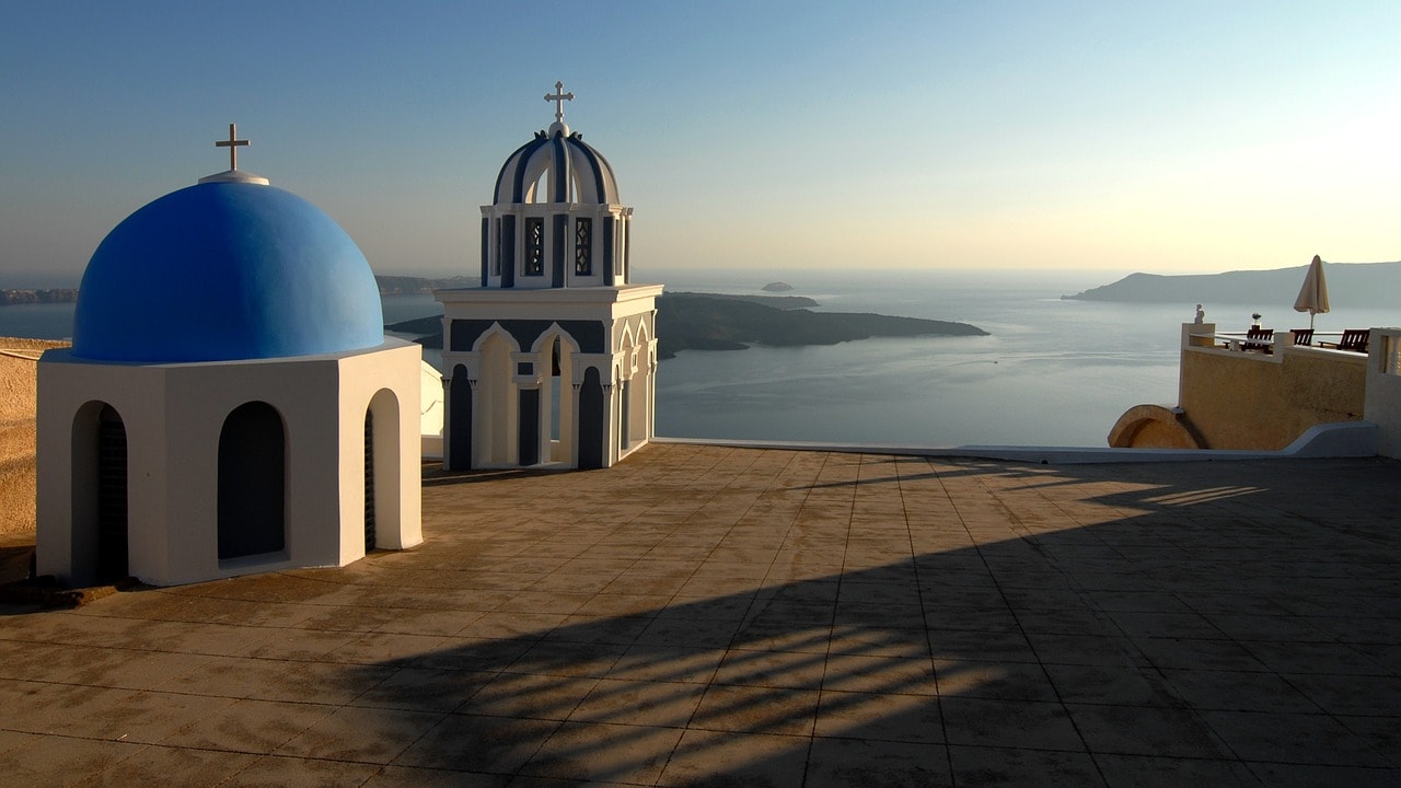 Un vol Grèce pas cher avec Algofly illustré par une église à coupole bleue en front de mer.