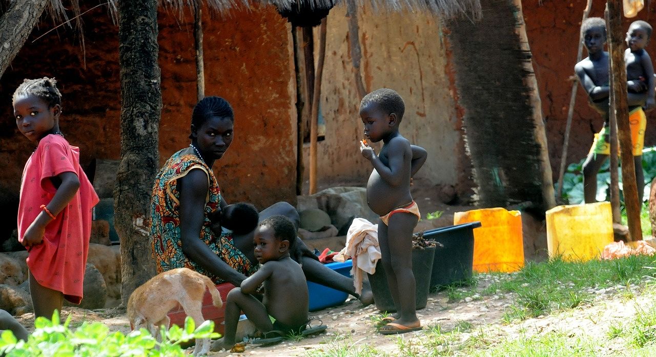 Un vol Guinée Bissau pas cher avec Algofly illustré par une maman et ses enfants devant leur maison.