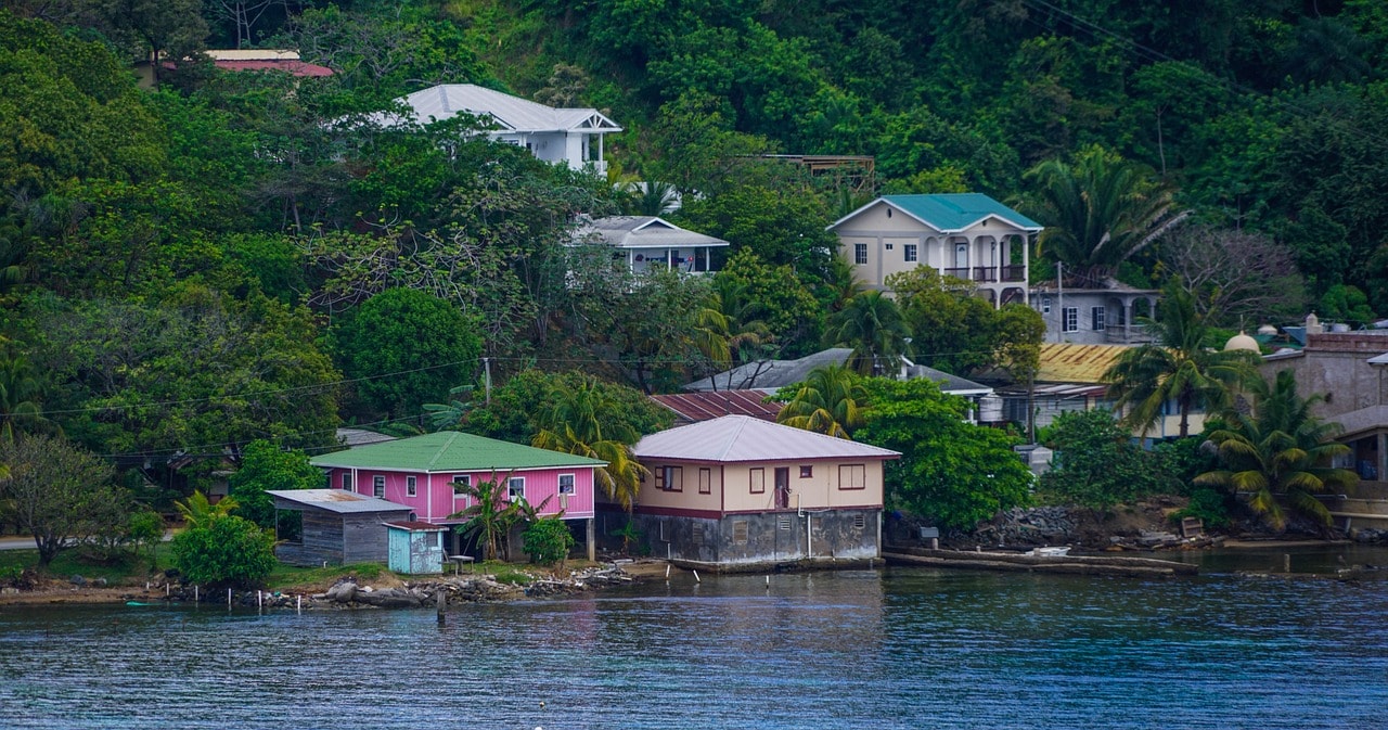 Un vol Honduras pas cher avec Algofly illustré par des maisons de couleur rose, blanche, bleu et verte au bord de l'eau.