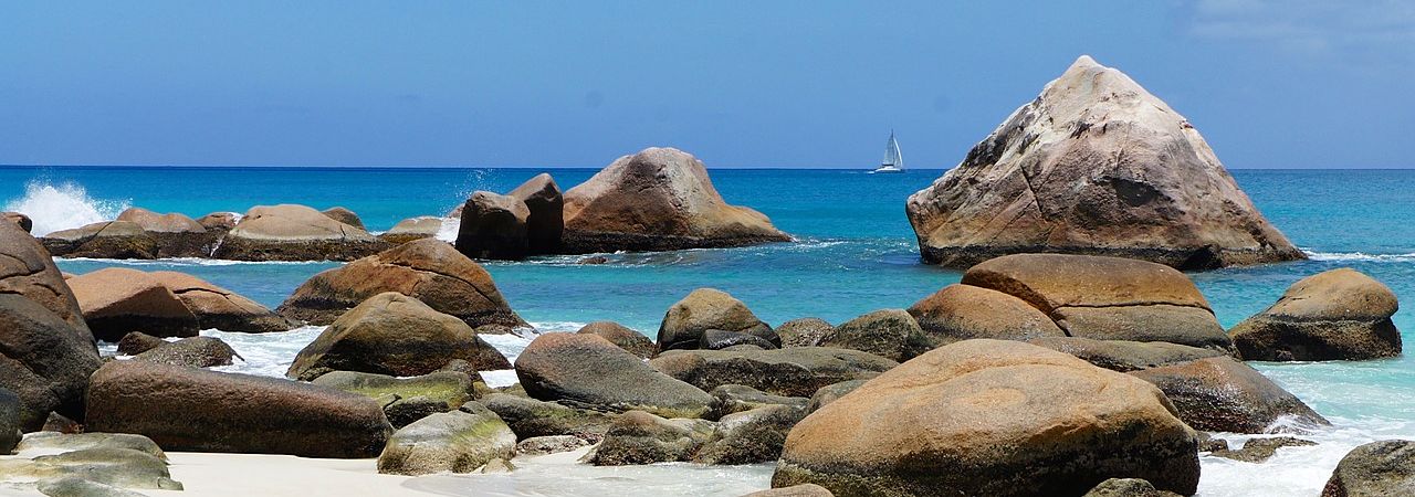 Un vol Seychelles pas cher avec Algofly illustré par des rochers polis au bord d'une mer bleue nuancée.
