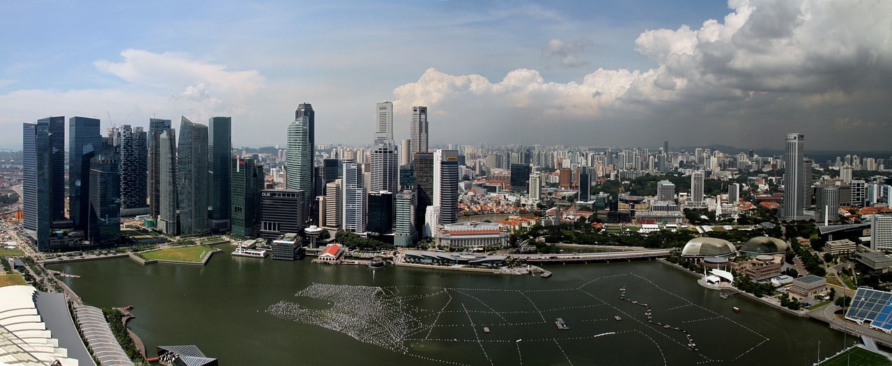 Un vol Singapour pas cher avec Algofly illustré par ses gratte-ciels et sa grande roue éclairée de nuit devant la baie de Marina Bay.