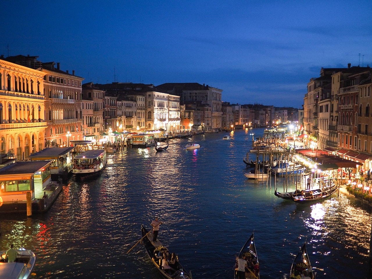 Un vol Venise pas cher avec Algofly illustré par des bateaux navigant de nuit sur le canal vu depuis un pont principal.